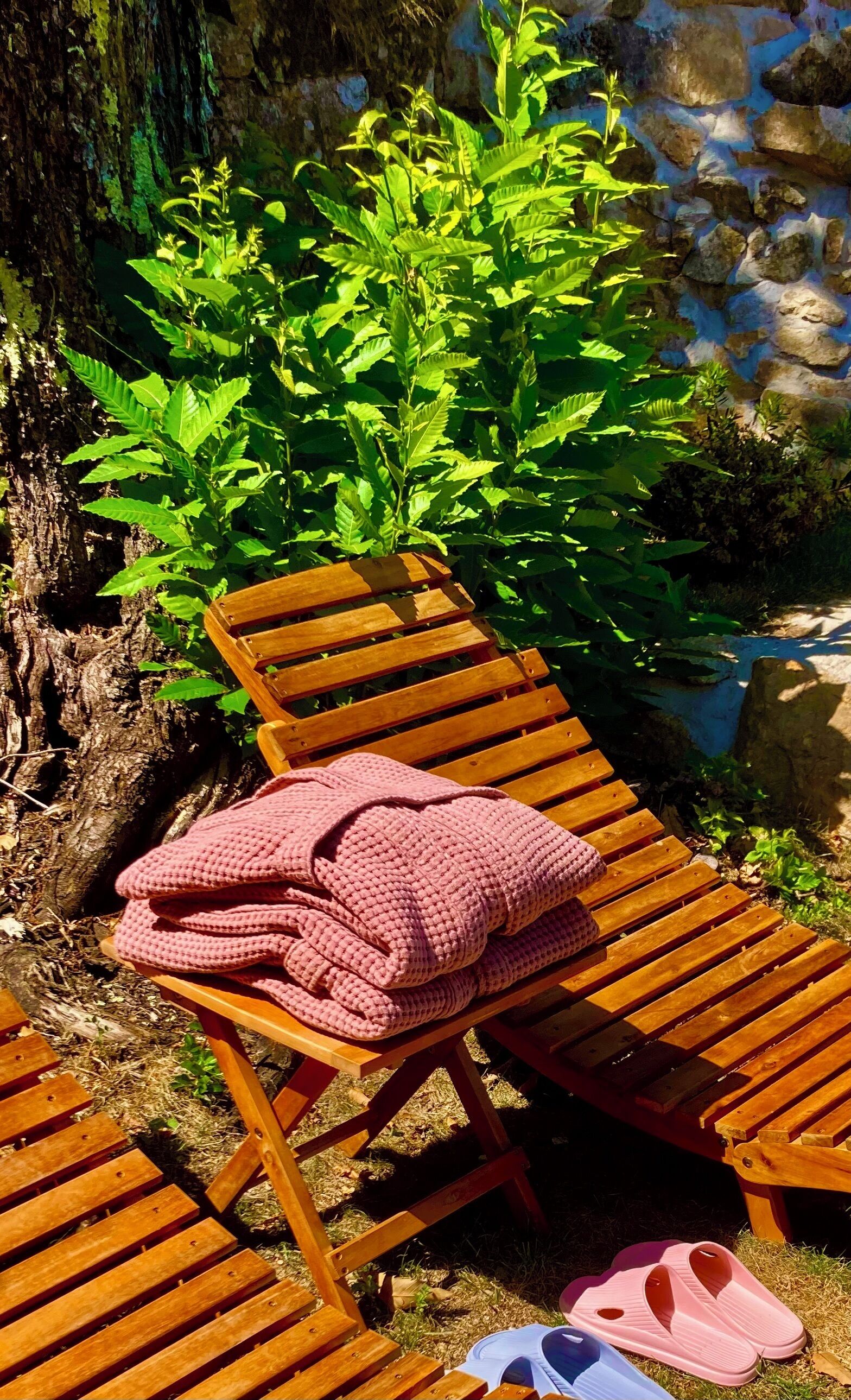 Eine Holzbank mit einer rosa Strickdecke und einem Paar rosafarbener Hausschuhe.