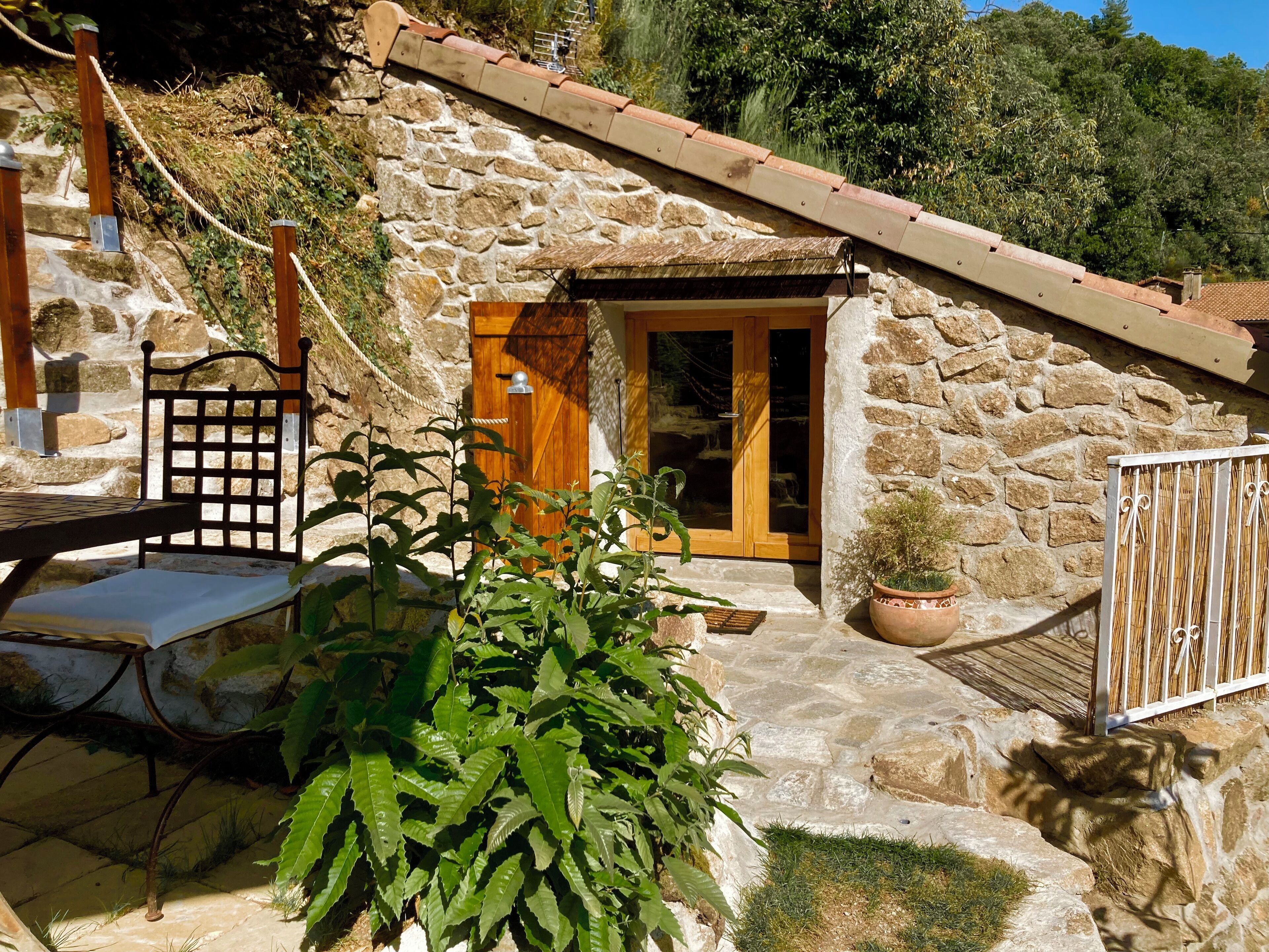 Une maison en pierre avec une porte en bois, un portail en métal et un banc.