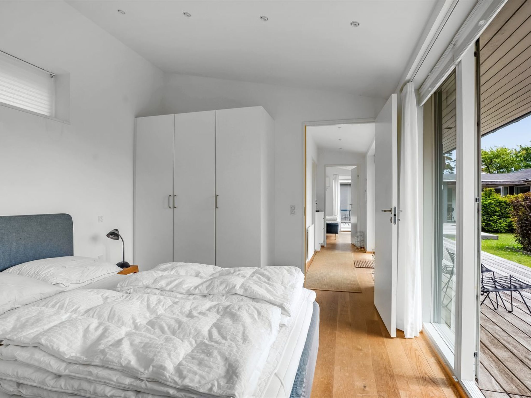A modern bedroom with a large bed, a wardrobe, and a view of the outdoor deck through a sliding glass door.