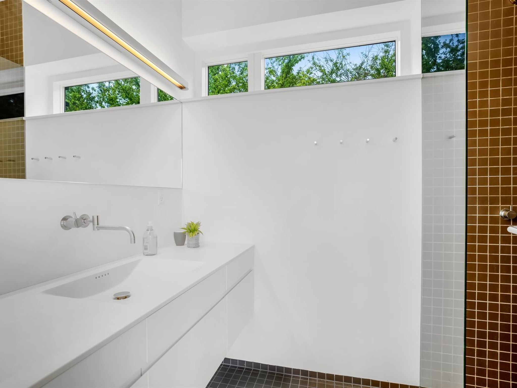 A modern bathroom with a large white sink, a mirror, and a shower area.