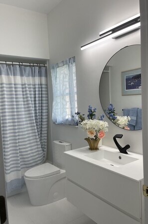 Bathroom features a toilet, sink, and mirror, with a window and framed artwork.