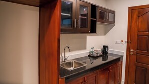 A kitchen with wooden cabinets, a black countertop, a stainless steel sink, and a coffee maker. - MarvelInn Siem Reap (Siem Reap)