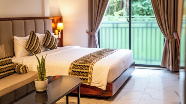 A hotel room with a bed, a bedside table with a plant, a lamp, and a view of a balcony. - MarvelInn Siem Reap (Siem Reap)