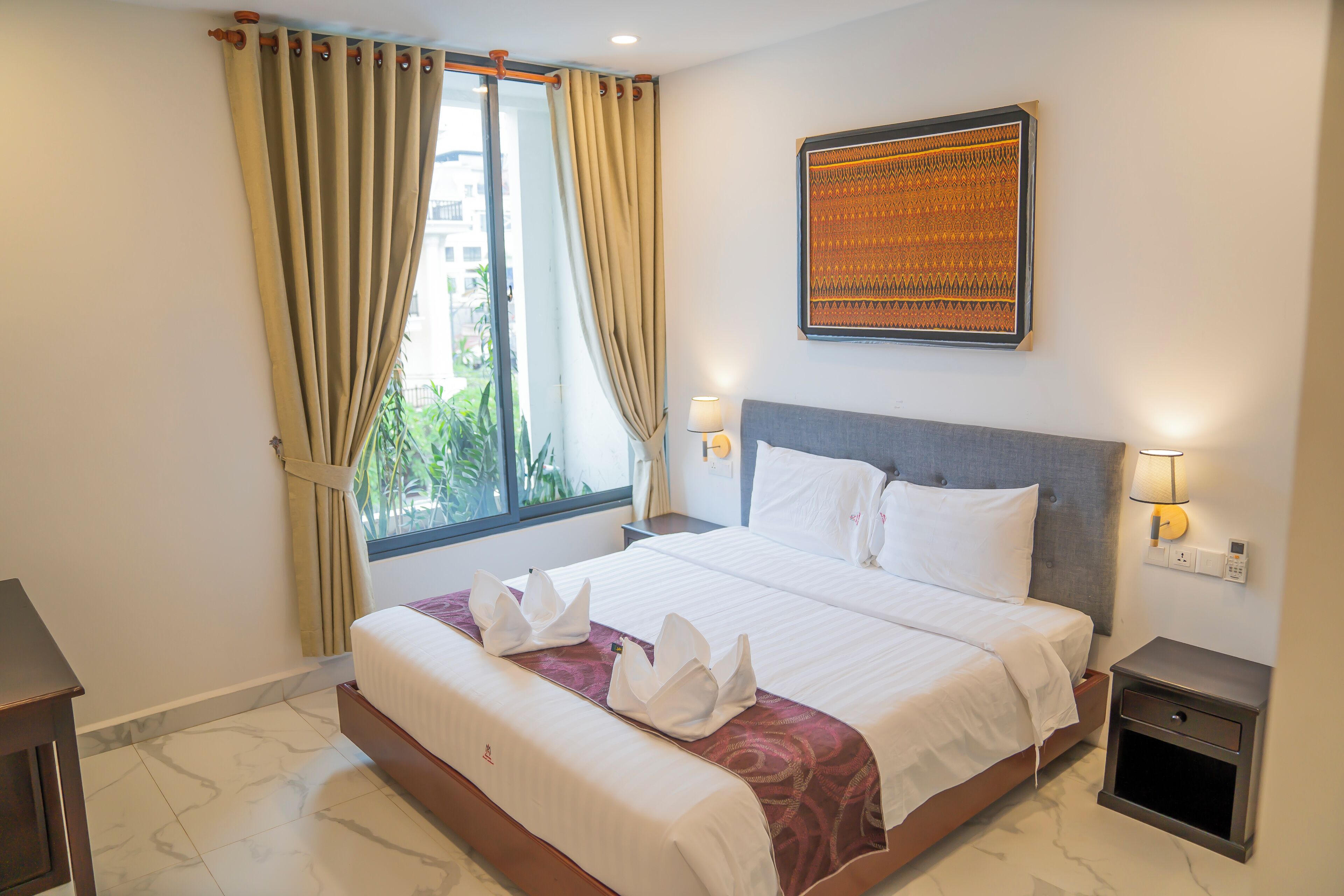 A hotel room with a large bed, a window with curtains, a wall-mounted artwork, and bedside lamps.