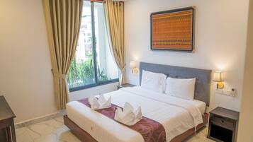 A hotel room with a large bed, a window with curtains, a wall-mounted artwork, and bedside lamps.
