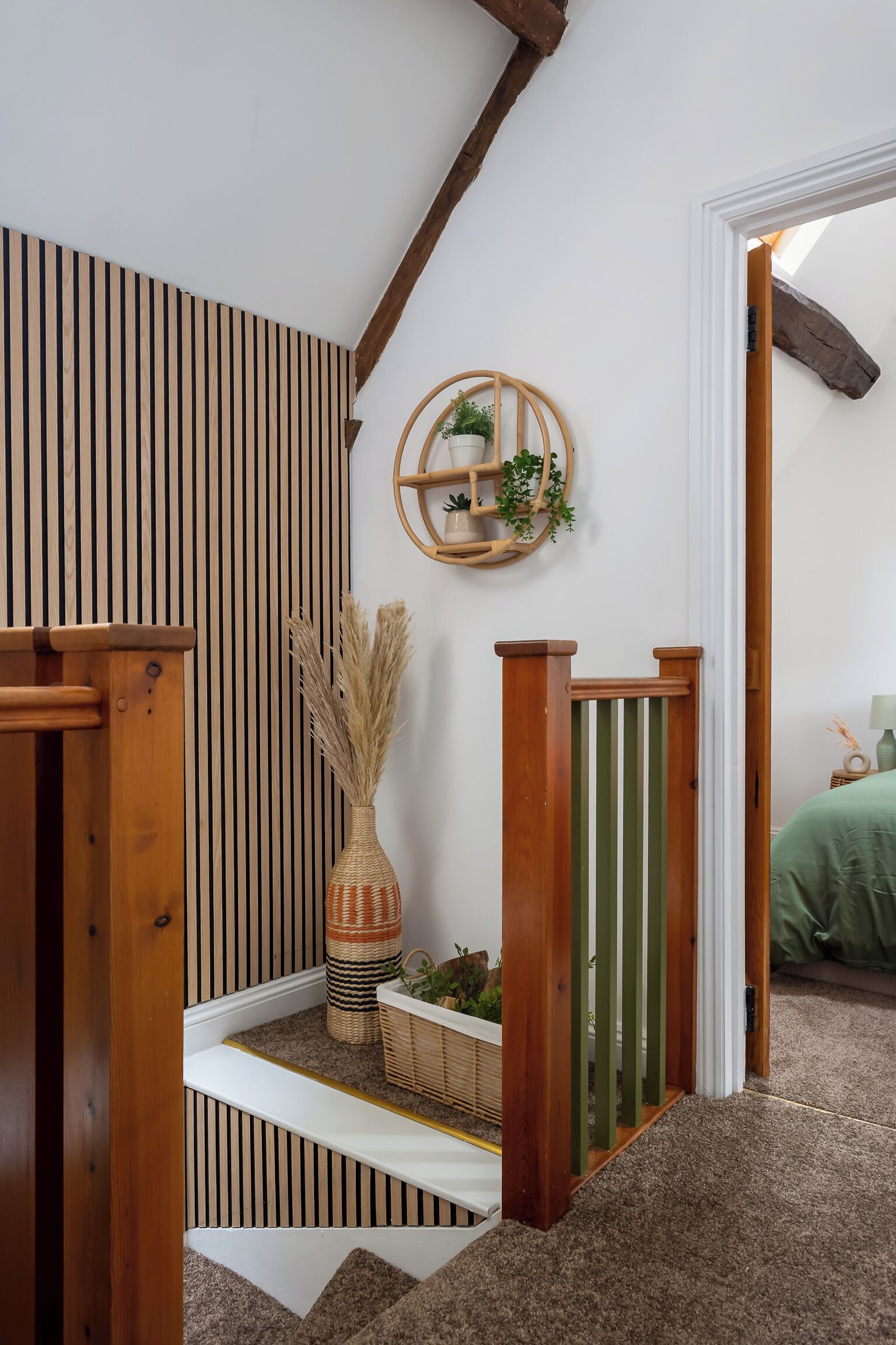 Una escalera con barandillas de madera y una pared blanca con rayas verticales. En la pared, hay un estante con plantas y un objeto decorativo.