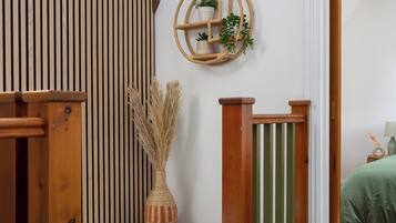 Una escalera con barandillas de madera y una pared blanca con rayas verticales. En la pared, hay un estante con plantas y un objeto decorativo.
