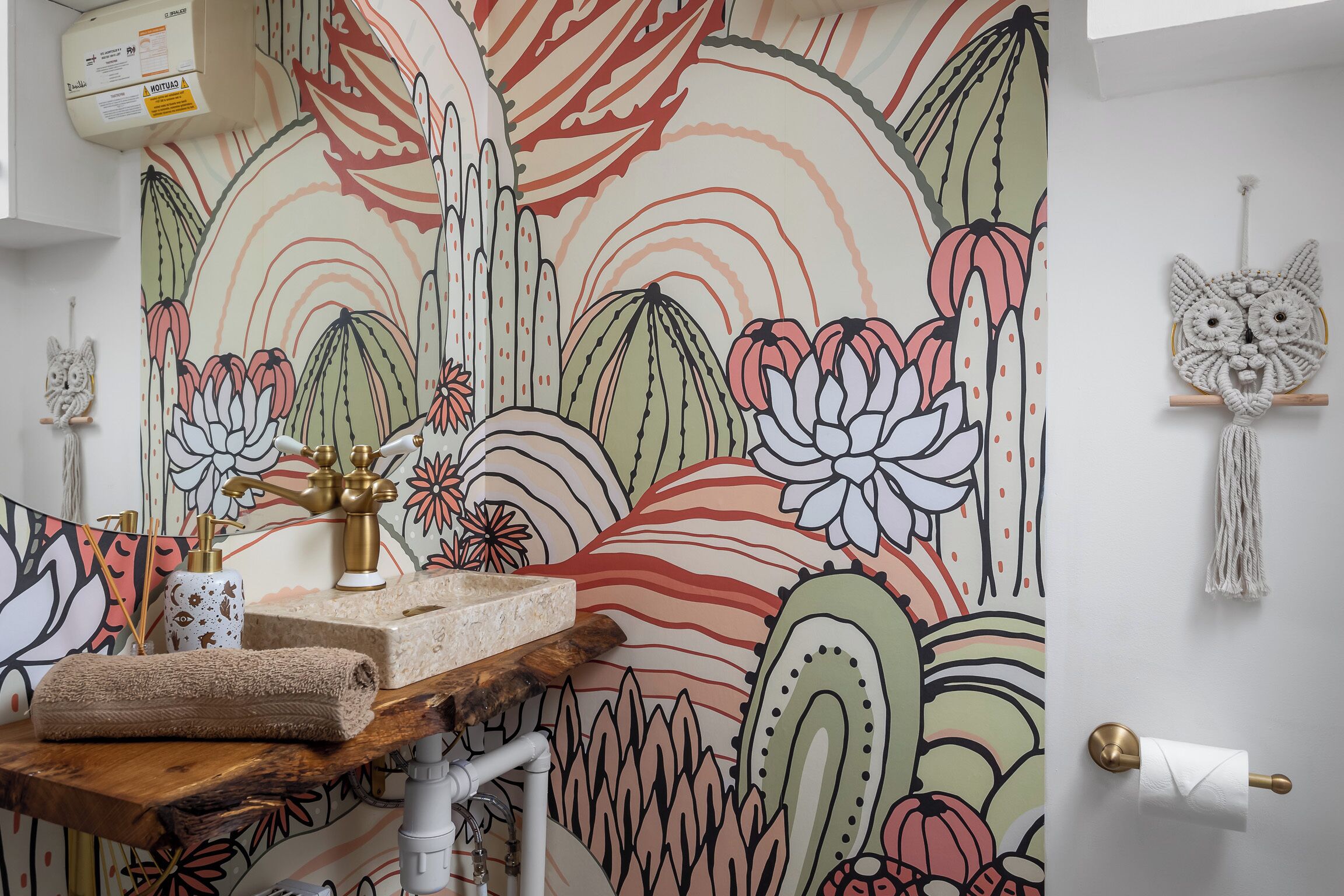 Ein Badezimmer mit floraler Wandmalerei, einem Holzkosmetikschrank, einem Waschbecken und einem Wandbehang aus Makramee.