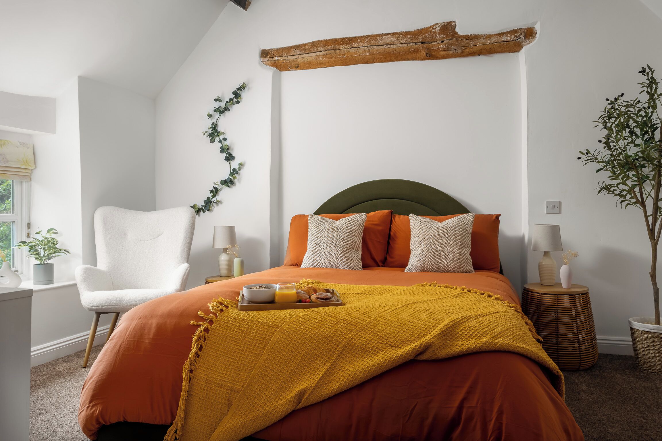 Un dormitorio con una cama, una silla, una mesita de noche, una lámpara y una planta.
