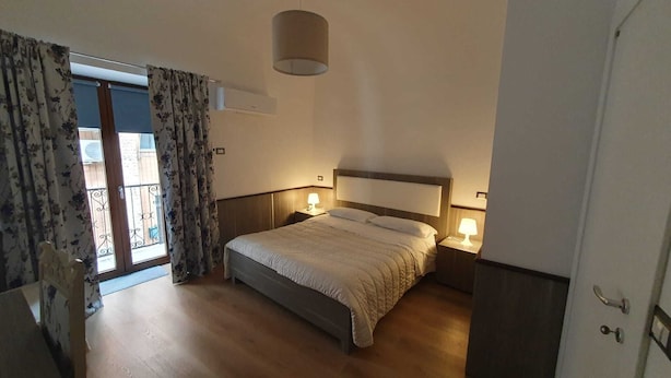 A bedroom with a bed, two bedside lamps, a ceiling light, a sliding glass door with curtains, and a wooden floor. - Detached house St. George in the heart of the country (Vallata)