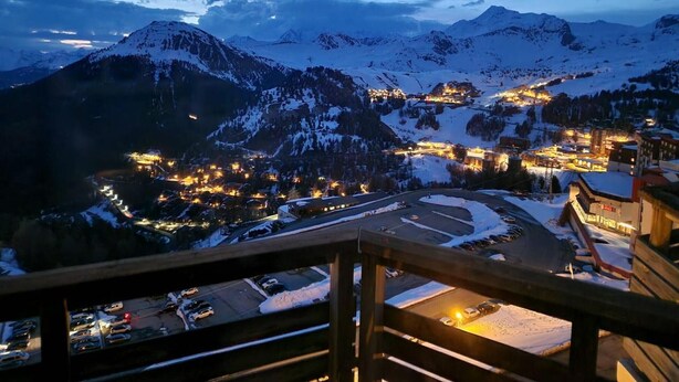 Eine verschneite Bergstadt im Abendlicht mit beleuchteten Häusern und Blick auf die umliegenden Berge.