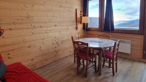 Ein Holzhütten-Zimmer mit Esstisch, Stühlen, einem Fenster mit Vorhängen und einem Heizgerät.