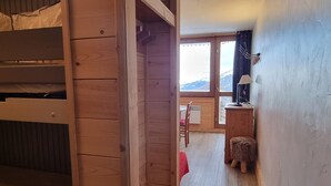 Ein Holzinterieur mit einem Etagenbett, einem Schreibtisch mit Lampe und Blick auf Berge durch ein Fenster.