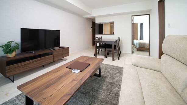 Un salón moderno con televisor de pantalla plana, mesa de centro de madera y sofá color beige.
