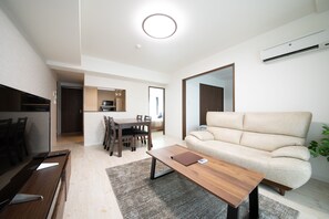 A modern living room with a sofa, a coffee table, a dining area with chairs, and a kitchen in the background. - OTARU SAMPO (Otaru)
