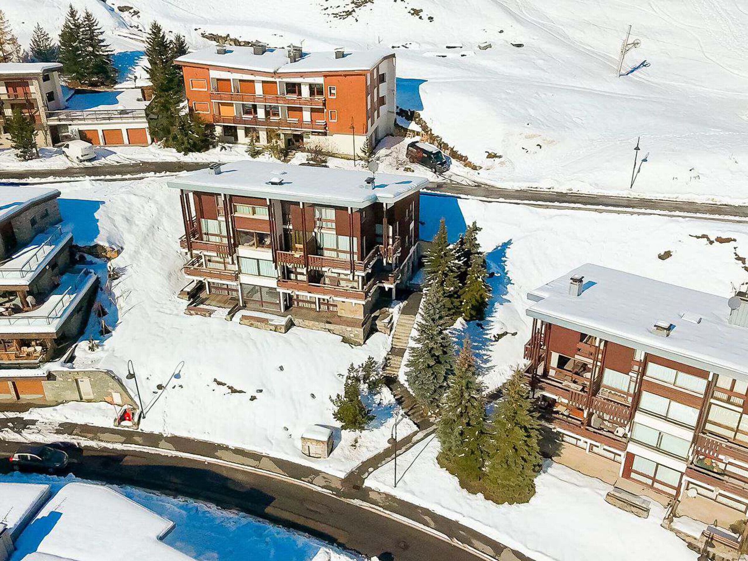 A multi-story hotel with balconies, a swimming pool, and a ski lift in the background.