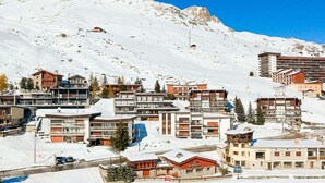A snow-covered mountain town with modern buildings, a small lake, and a clear blue sky.