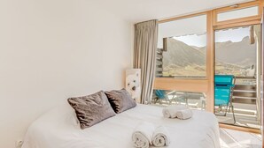 A bedroom with a large bed, a view of mountains through a sliding glass door, and a balcony with a blue chair.