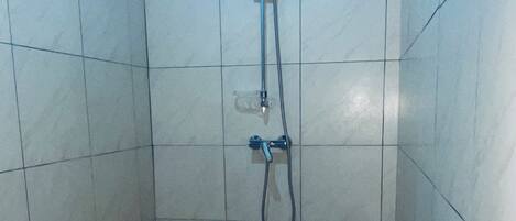 A small, tiled bathroom with a toilet, a shower, and a wall-mounted faucet.