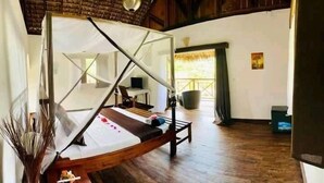 Una habitación con cama, piso de madera, pared blanca, ventana y puerta.