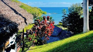 Un paisaje tropical con vista despejada al océano, una estructura de techo de paja y abundante vegetación.