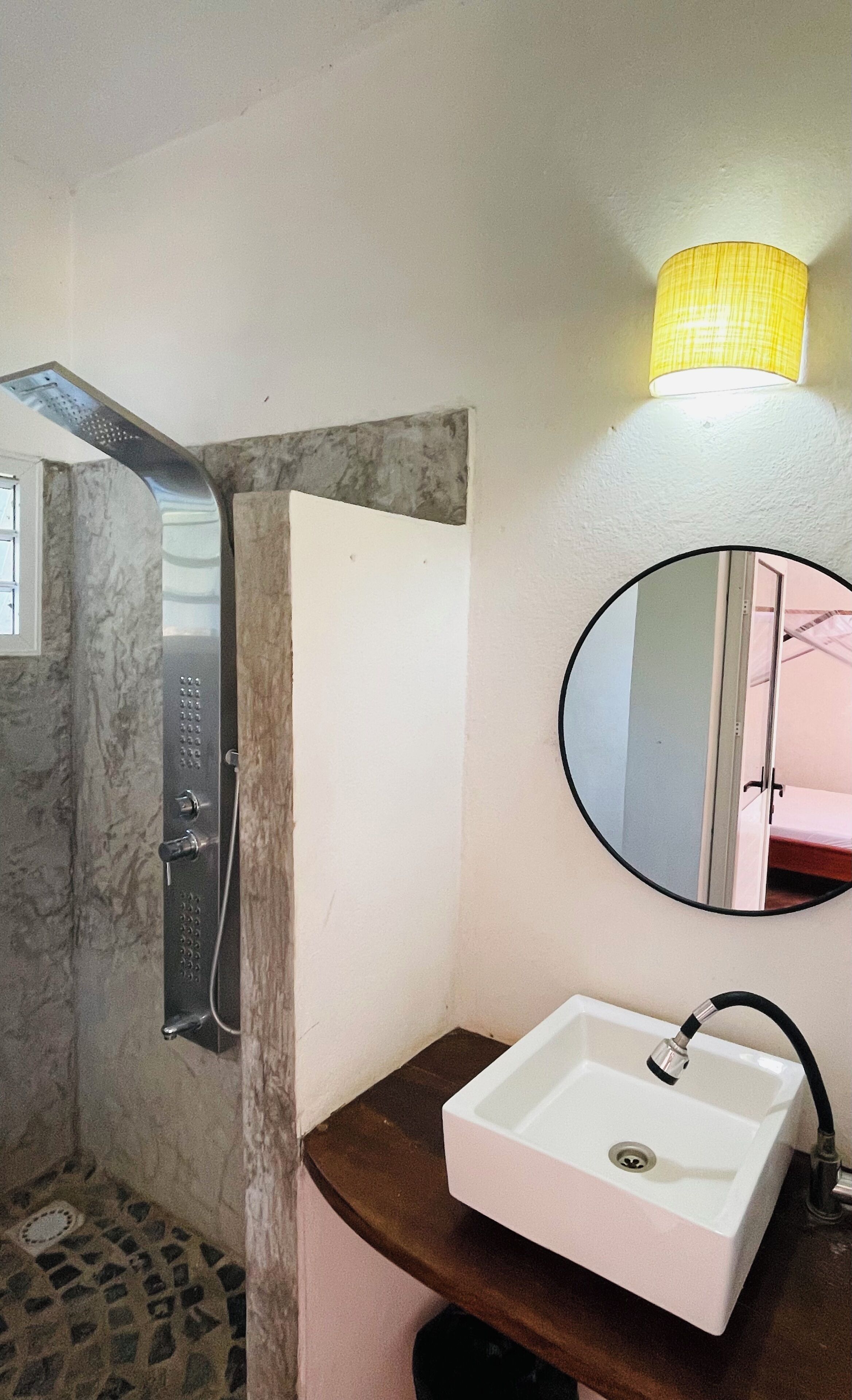 A bathroom with a shower, a sink, a mirror, and a wall-mounted lamp.