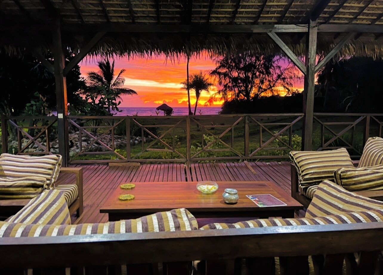 An outdoor seating area with wooden furniture and a view of a sunset over the ocean.