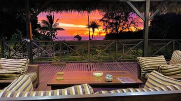 An outdoor seating area with wooden furniture and a view of a sunset over the ocean.