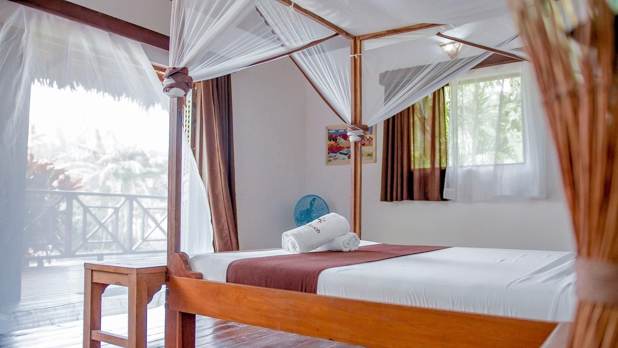 A four-poster bed with white linens, a wooden headboard, and a red throw blanket.