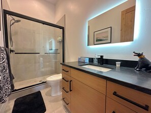 A modern bathroom with a glass shower enclosure, a white toilet, and a wooden vanity with a black countertop.