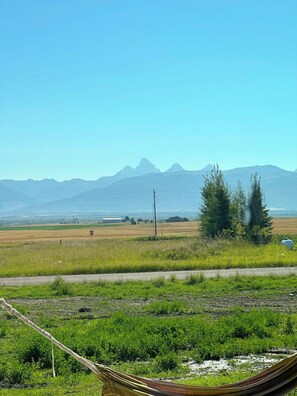 A rural landscape with a clear sky, distant mountains, and a road with a hammock in the foreground.