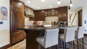 Una cocina moderna con armarios de madera oscura, una isla grande con taburetes de bar, un microondas de acero inoxidable y un perchero para esquíes.