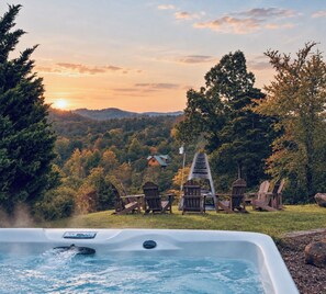 A hot tub with a view of a forest and a house in the background.