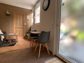 Une pièce avec une porte en bois, une table à manger avec des chaises, une petite table d’appoint, une horloge au mur et une porte en verre dépoli.