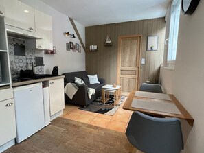 Een compacte woonruimte met een kitchenette, een bank, een eettafel en een houten deur.