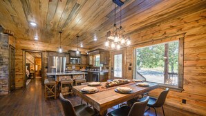 Ein Holzinterieur mit einem für vier Personen gedecktem Esstisch, einer Küchenzeile und großen Fenstern.