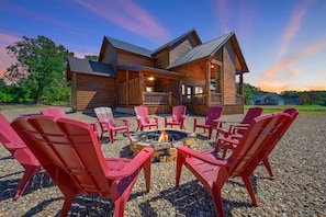 Une cabane en rondins avec un foyer et des chaises Adirondack rouges devant.