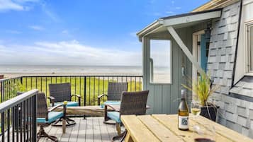 Une terrasse en bois avec des chaises et une table en osier, donnant sur une plage.