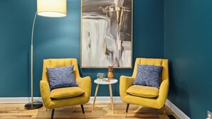 Een kamer met turquoise wanden, twee gele fauteuils met blauwe kussens, een vloerlamp en een kleine tafel met decoratieve objecten.