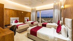 A hotel room with four beds, a desk, a chair, and a balcony with a view. - Gaurison Hotel&Resort (Ujjain)