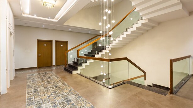 A modern interior with a glass staircase, a patterned floor, and a ceiling light fixture. - Gaurison Hotel&Resort (Ujjain)