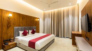 Habitación de hotel moderna con una cama grande, paneles de madera, ventilador de techo y televisor montado en la pared.