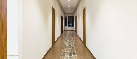 A long, narrow hallway with patterned tiles on the floor, white walls, and wooden doors on both sides.
