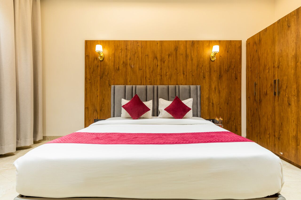 Ein großes Bett mit grauem Polsterkopfteil, zwei roten Kissen und einer weißen Bettdecke. An beiden Seiten des Kopfteils befinden sich zwei Wandleuchten.