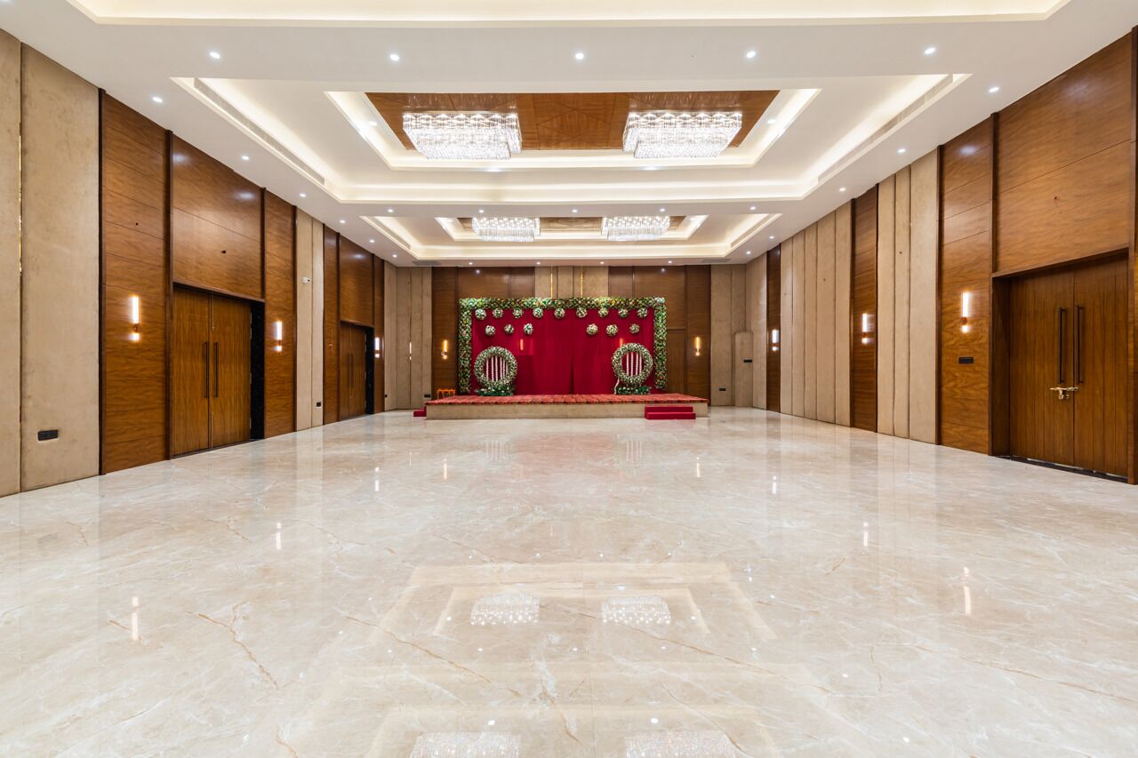 A spacious, well-lit conference room with a polished marble floor, wooden paneling, and a stage with red curtains and floral decorations.