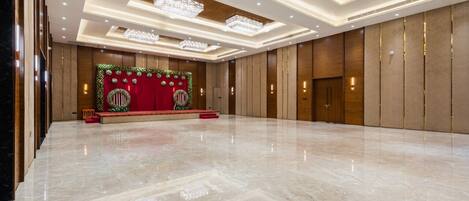 Una espaciosa sala de conferencias, bien iluminada, con un escenario, candelabros y un suelo de mármol pulido.