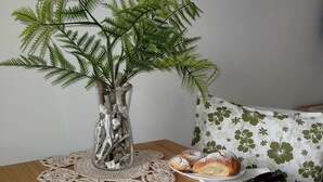 Una mesa de comedor con pasteles, un florero con una planta y un cojín estampado con motivos florales.