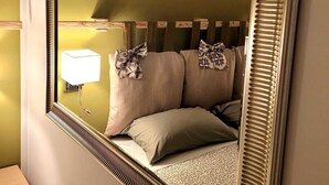 Un dormitorio con un espejo grande, una cama con dos almohadas, una lámpara de noche y una mesita de noche.