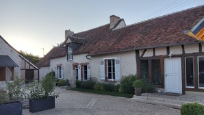 Un bâtiment de style européen traditionnel, avec un toit en tuiles, des volets blancs et une cour recouverte de gravier.