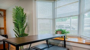 Una habitación moderna con una mesa de madera, un banco tapizado negro y ventanas amplias con persianas.
